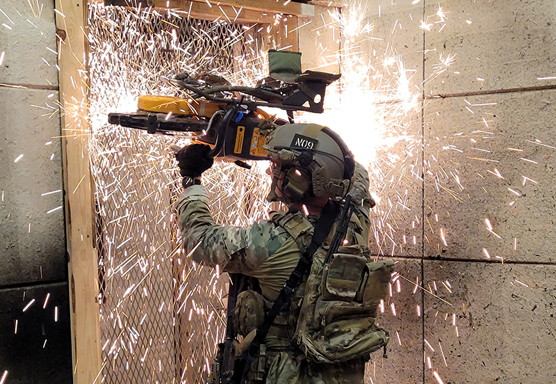 A Special Forces operator utilizes a quickie saw to bypass an obstacle while conducting close quarters combat. 